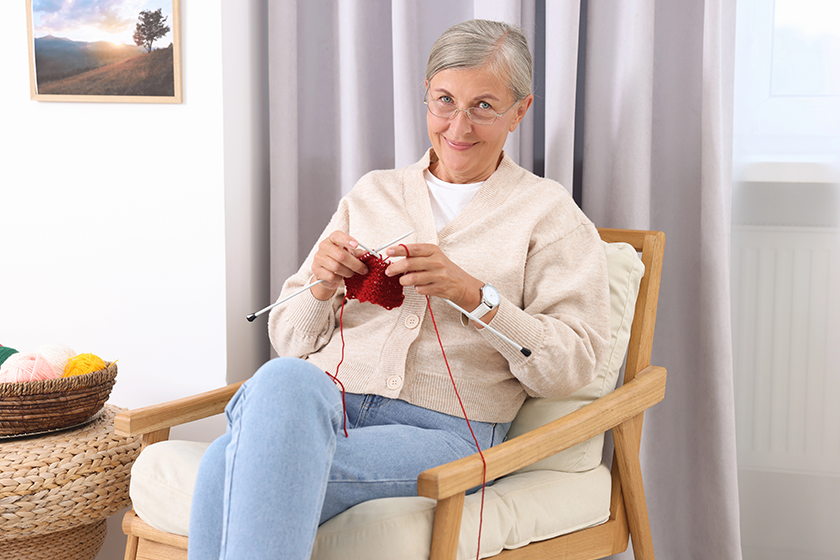 Beautiful senior woman knitting on armchair 