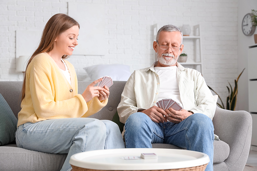 Female caregiver with senior man playing cards 