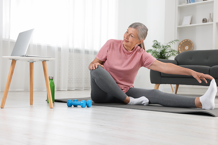 Senior woman in sportswear stretching on fitness mat